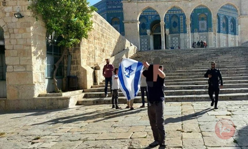 A settler raises the flag of Israel during his storming Al-Aqsa Mosque